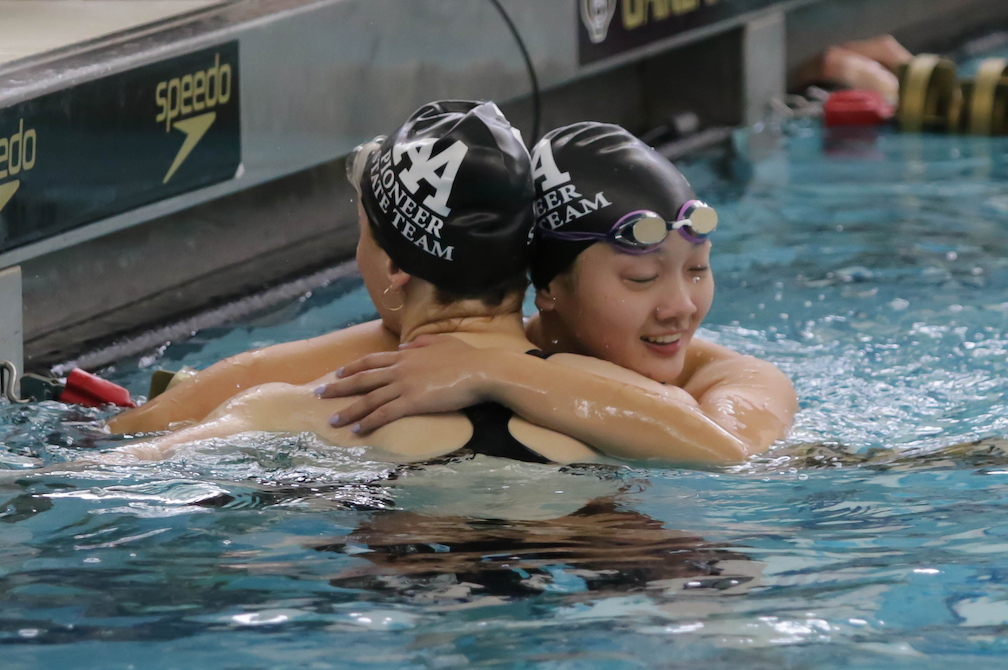 Ann Arbor Pioneer’s Sophia Guo, right, embraces teammate Lucy Mehraban after their 100-yard freestyle race Saturday. 