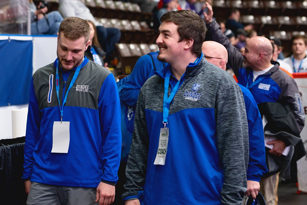 Nate Hall, left, and Garrett Stevens walk together during the opening march at an MHSAA Team Finals; retired coach Tim Roberts is behind them, waving. 