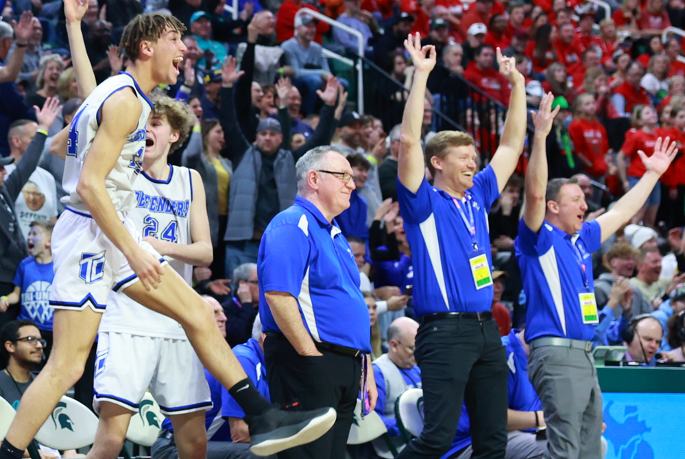 The Wyoming Tri-unity Christian bench, including the author (far right) and head coach Mark Keeler (middle), celebrate a 3-pointer late in the Defenders’ Division 4 championship win over Mount Pleasant Sacred Heart. 