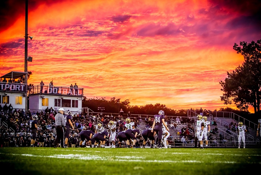 This photo shows Muskegon Catholic Central playing football at Fruitport under a bright sunset. 