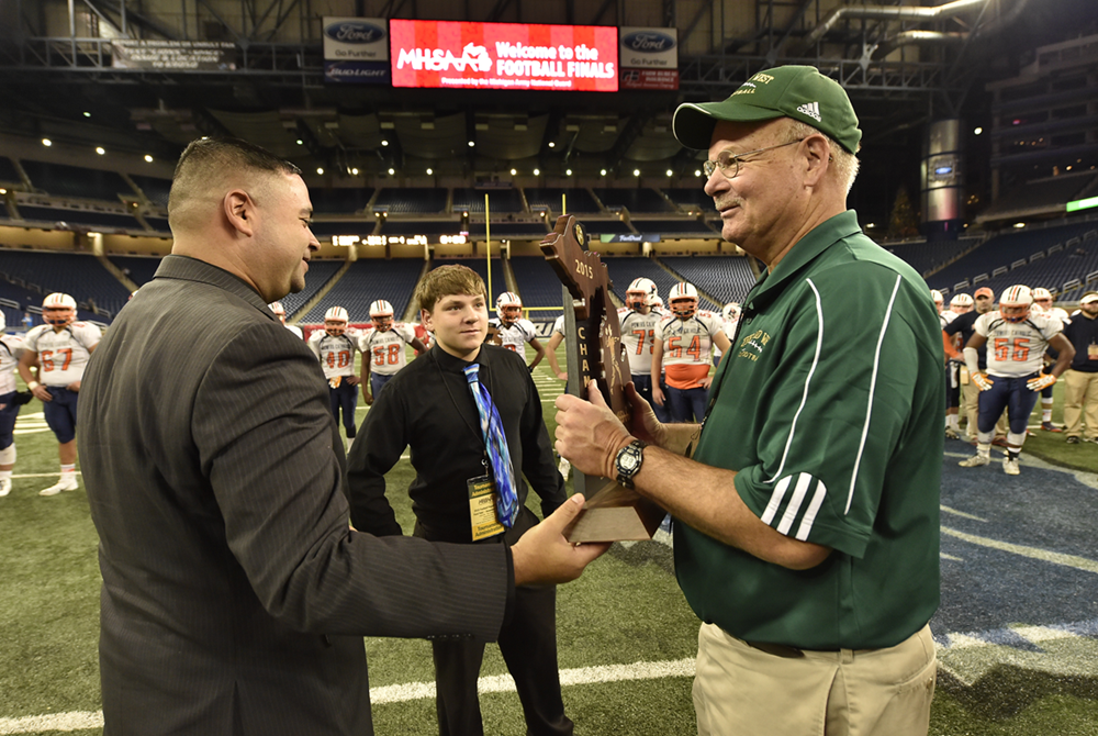 Zeeland West football coach John Shillito, right, receives the Division 4 championship trophy from MHSAA Representative Council member Orlando Medina in 2015 at Ford Field.