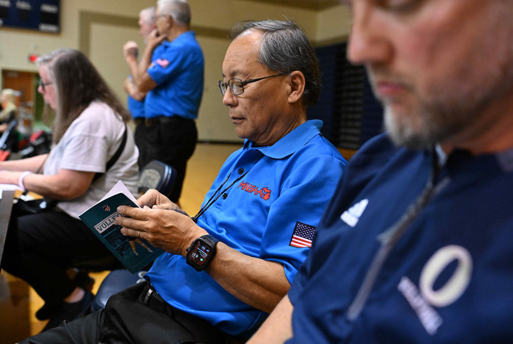 An MHSAA volleyball official is seated and looking something up in an NFHS rulebook. 