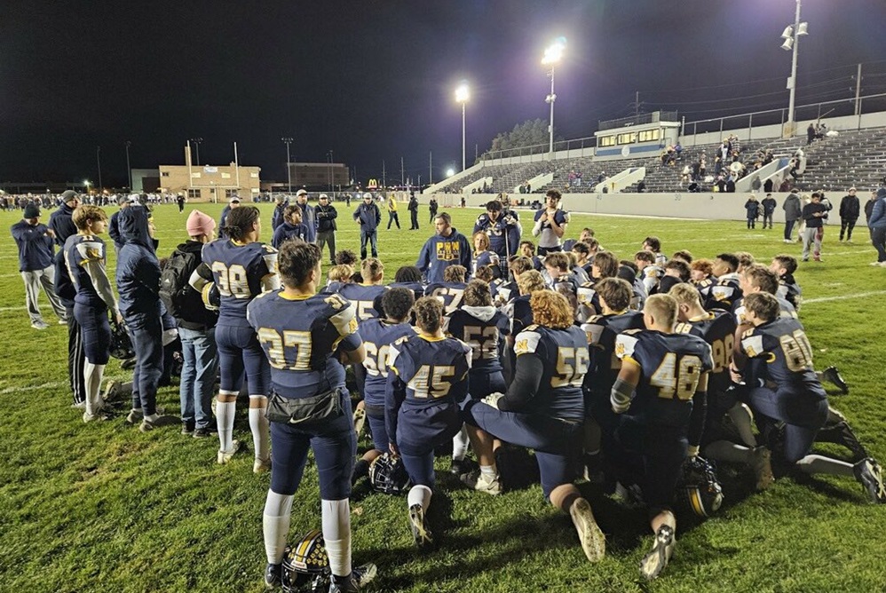 Port Huron Northern football coach Larry Roelens, middle, is surrounded by his kneeling players during a postgame huddle.