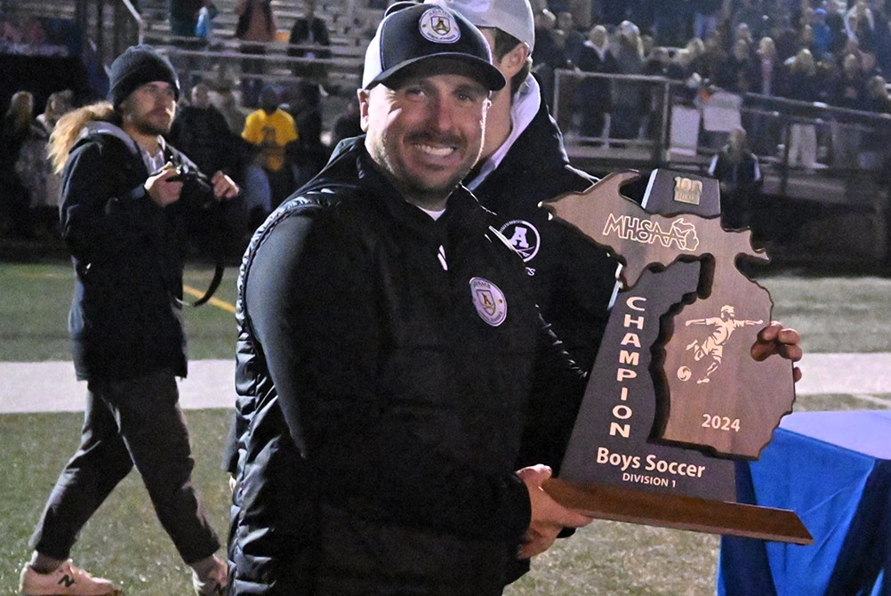 Rochester Adams soccer coach Josh Hickey shows the Division 1 championship trophy after his boys team defeated Byron Center on Nov. 2 at Grand Ledge High School.