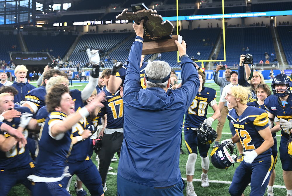 Goodrich football coach Tom Alward hoists his football program’s first championship trophy as players rush to him Saturday at Ford Field. 