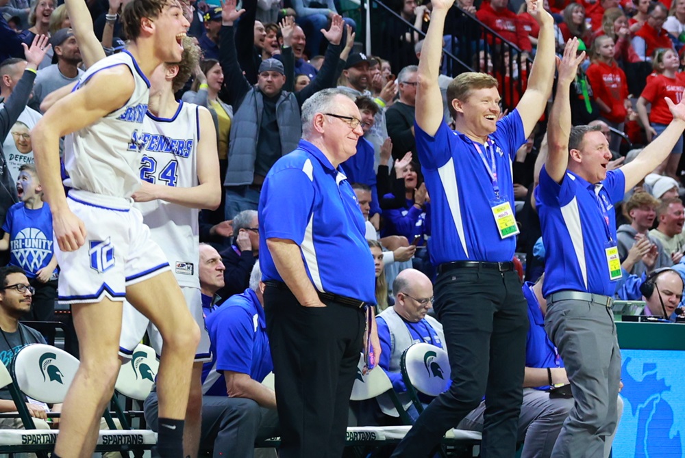 Surrounded by celebrating players and assistant coaches (including the author, far right), Tri-unity boys basketball coach Mark Keeler (hand in pocket) enjoys a  moment near the end of last season’s Division 4 championship game. 