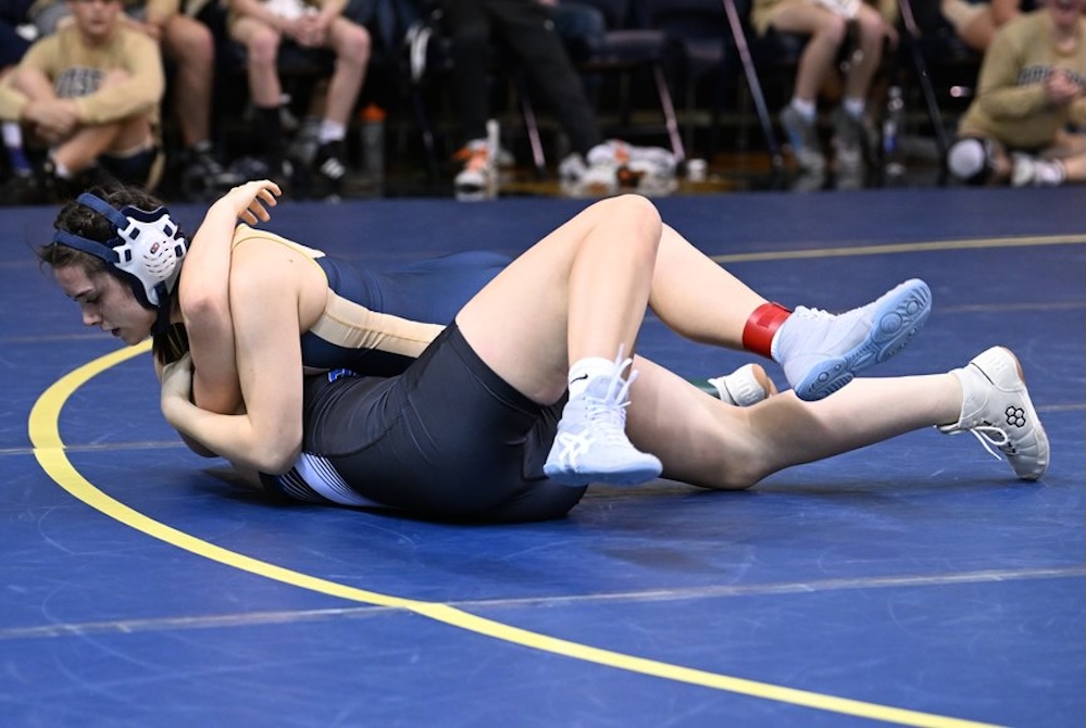 Wrestlers compete on the mat near the boundary line during a December match.