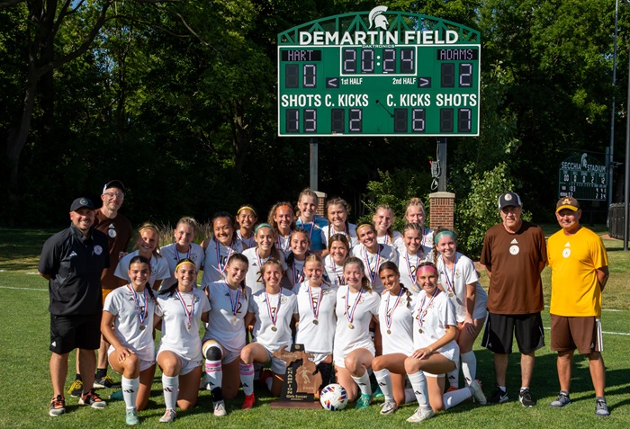 Hickey, far left, takes his spot in the team photo after Adams’ girls won the Division 1 title in June at Michigan State’s DeMartin Stadium.