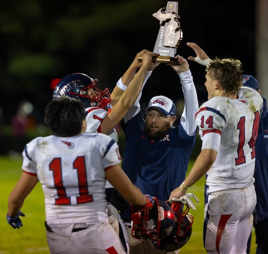 Ramblers coach Dave Suttle, middle, raises the District championship trophy with senior Leon Xiong (11) and junior Owen Hewitt (14).