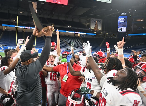 St. Mary’s coach Jermaine Gonzales raises the championship trophy as his players cheer.