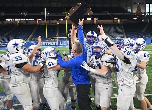 Aggies coach Brad Antcliff raises the Division 8 championship trophy as his players celebrate.