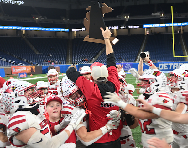 Millington coach Jason Germain holds up the championship trophy as he’s embraced by one of his players. 