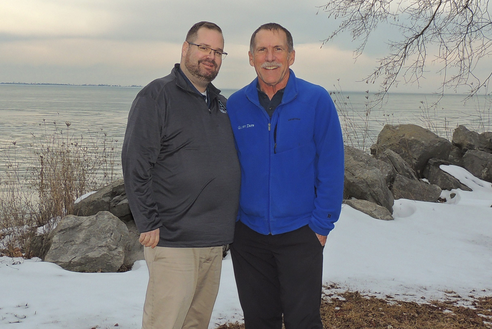 Alpena athletic director Jon Studley, left, and retired MHSAA game official Dan Godwin take a photo together on the shore of Lake Huron one year after Godwin donated a kidney to Studley. 